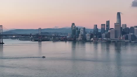 Aerial-back-subject-view-along-San-Francisco-Bay-with-skyline-in-background-at-sunrise