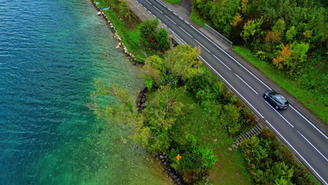 Aerial-view-of-cars-driving-by-a-lakeside-road-flanked-by-colorful-autumn-trees