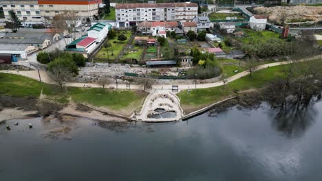 Thermal-pool-and-park-area-at-Chavasqueira-along-river-in-Ourense-Galicia-Spain,-aerial-pullback