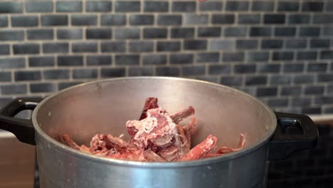 Hand-adding-raw-fresh-beef-bones-to-pan-for-cooking-bone-broth,-slow-motion