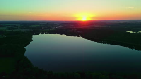 Aerial-shot-flying-backward-revealing-a-serene-lake-at-sunset-surrounded-by-trees-with-vibrant-sky-colors-reflected-in-the-water