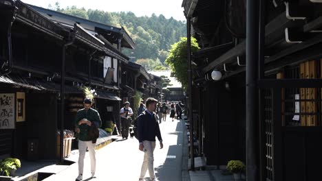 Two-young-tourists-walking-among-the-people-in-the-alley-of-a-retro-Japanese-market,-in-Takayama,-look-and-enter-the-shops-and-businesses