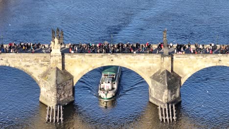 Tourist-boat-slowly-float-on-river-under-crowded-Charles-bridge-with-people