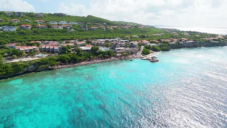 Panoramic-drone-rises-above-stunning-clear-blue-ocean-water-to-reveal-luxury-villas