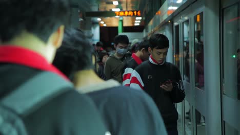 Row-of-young-adult-Asian-men-politely-waiting-on-subway-platform-handheld