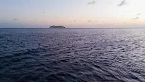 Low-flying-aerial-dolly-to-cruise-ship-in-open-ocean-at-dusk,-stunning-cinematic-sunset