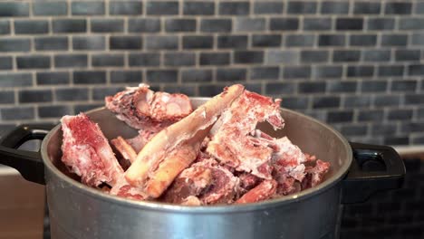 Slow-motion-Heap-of-Raw-Beef-Bones-falling-into-Kettle-on-Stove