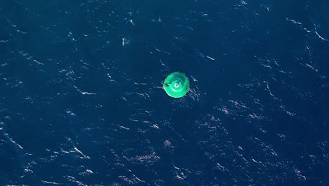Drone-top-down-satellite-view-of-large-green-navigation-buoy-bobbing-in-open-ocean-water
