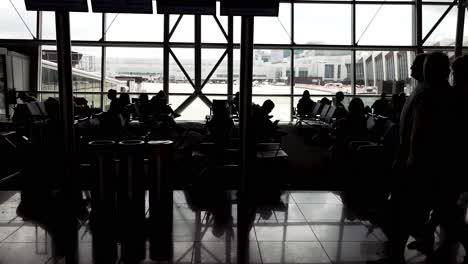 Filmische-Ansicht-Von-Reisenden-In-Silhouette,-Die-Tagsüber-In-Der-Flughafenlounge-Warten-Und-Spazieren-Gehen