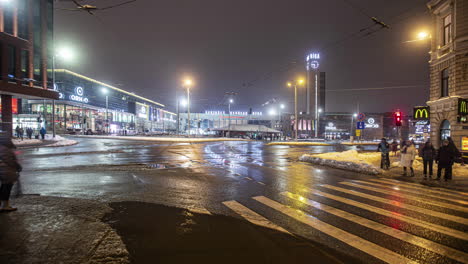 Timelapse-shot-of-pedestrians-crossing-city-street-intersection-along-wet-roads-caused-due-to-melting-snow-at-night-time