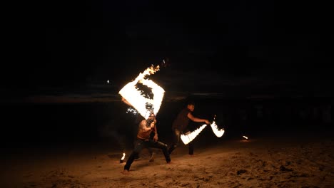 Fire-dancers-perform-a-night-show-on-a-sandy-beach-in-Krabi-Thailand,-with-dynamic-flames-against-dark-backdrop
