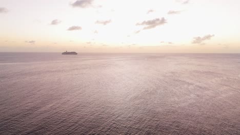 Aerial-orbit-around-open-ocean-shimmering-at-sunset-golden-hour-with-cruise-ship-in-distance