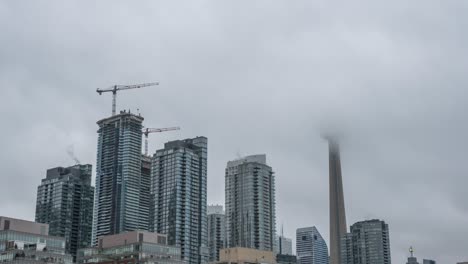 Time-lapse-shot-of-flying-grey-clouds-over-skyscraper-during-construction-site-in-Downtown-Toronto,-tilt-up-bottom-shot