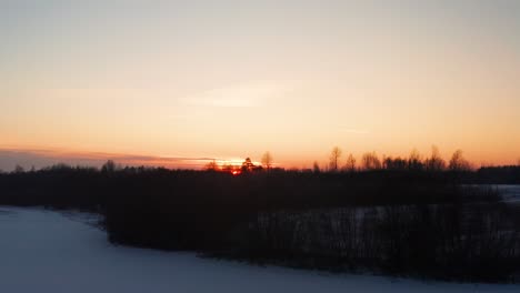 Luftaufnahme-Eines-Farbenfrohen-Sonnenuntergangs-über-Einem-Schattigen-Wald-Und-Einem-Verschneiten-Landwirtschaftlichen-Feld