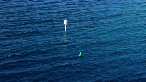 Tall-white-buoy-bobs-in-middle-of-deep-blue-ocean-water-with-whitecaps