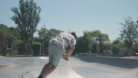 Young-male-athlete-perform-tricks-with-stunt-scooter-at-skatepark-bowl