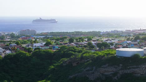 Aerial-orbit-around-local-coastal-town-with-large-cruise-ship-entering-port,-Seri-Domi-Curacao