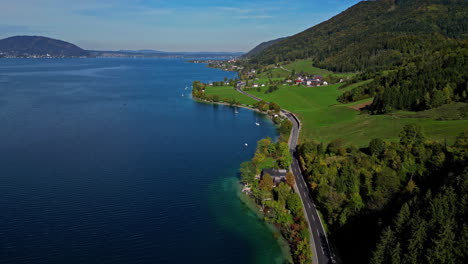 Aerial-view-following-a-road-on-the-coastline-of-lake-Attersee,-sunny-Austria