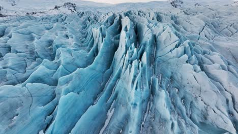 Aerial-view-over-textured-ice-formations-of-a-glacier-in-Iceland,-at-sunset