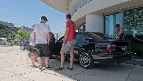 People-stood-around-a-black-BMW-M5-E39-Car-talking-at-museum-in-Munich,-Germany