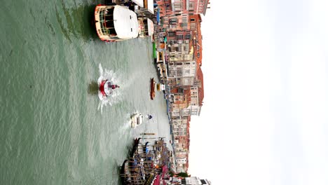 Man-navigates-motor-boat-in-bustling-Grand-Canal-near-Ponte-Rialto,-Venice