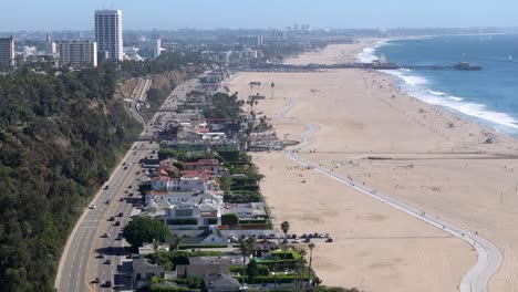 Large-beach-front-Houses-In-Santa-Monica-along-highway-101-on-an-overcast-day-with-famous-pier-off-in-a-distance,-4K-Drone-Flyover