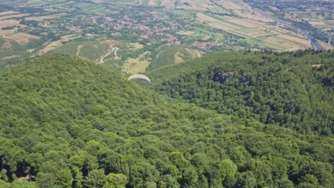 Scenic-view-of-paragliding-over-green-trees-with-valley-and-town-at-base-of-mountain