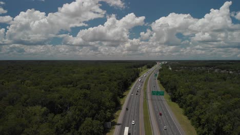 Drone-Aerial-pan-up-shot-revealing-the-highway-and-roads-cars-passing-by-blue-sky-white-clouds-trees-in-on-side-of-highway