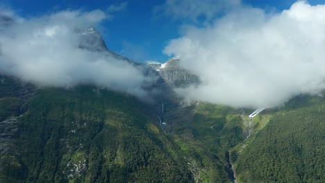 Pan-motion-flight-revealing-the-thick-clouds-covered-mountain-tops-and-waterfalls-rush-down-the-forest-covered-slope