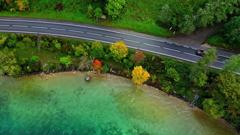 Car-driving-on-remote-lakeside-road,-aerial-top-down-view