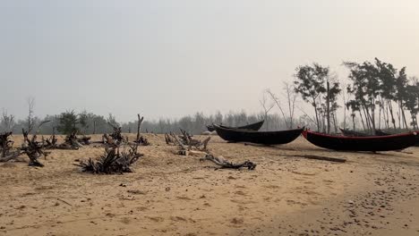 Panorama-shot-of-few-fishing-boats-kept-near-the-coastline-on-an-empty-barren-beach-during-sunset-in-Bengal,-India