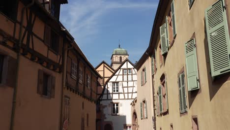 Half-timbered-architectural-buildings-in-Kaysersberg,-France,-church-clocktower-in-background