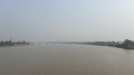 Cinematic-shot-of-a-muddy-river-flowing-down-a-bridge-joining-two-lands-with-industries-in-Bengal,-India