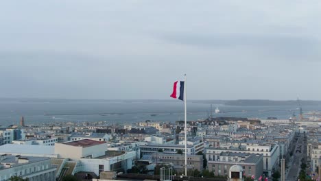 Majestätische,-Weiche-Luftumlaufbahn-Um-Die-Französische-Flagge-Mit-Der-Skyline-Von-Brest,-Frankreich-Im-Hintergrund