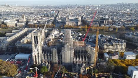 Drone-moving-forward-approaching-Notre-Dame-church-in-Paris-during-renovation,-many-cranes