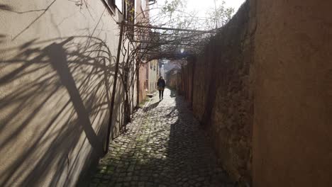 Woman-walking-alone-in-small-cobblestone-street-in-medieval-touristic-town-in-France,-Kaysersberg