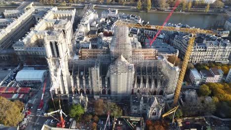 Drone-with-movement-backwards-away-from-the-Notre-Dame-church-in-Paris-during-renovation,-many-cranes,-Seine-river-in-the-background