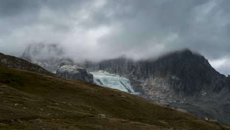 Storm-clouds-swirl-Rhone-Glacier-as-sunlight-dances-on-meadow,-Furkapass-Switzerland
