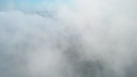 Aerial-view-through-a-thick,-white-fog-cloud-above-the-sea-on-a-sunny-morning