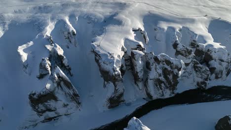 Aerial-panoramic-view-over-a-glacier-river-flowing-through-a-canyon-covered-in-snow,-on-a-sunny-day