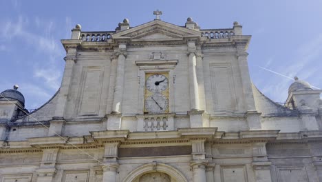 Frente-A-Un-Edificio-De-Iglesia-En-Un-Pequeño-Pueblo-De-Francia-Hecho-De-Piedra-Arenisca-Con-Un-Gran-Reloj,-Algunas-Columnas-Y-Decoraciones