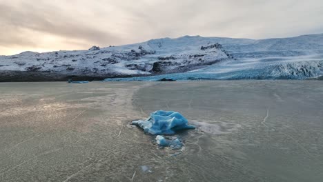 Aerial-landscape-view-over-an-iceberg-near-a-melting-glacier-with-ice-formations,-in-Iceland,-at-sunset