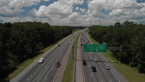 Drone-Aerial-pan-up-shot-revealing-the-highway-and-roads-cars-passing-by-blue-sky-white-clouds-trees-in-on-side-of-highway