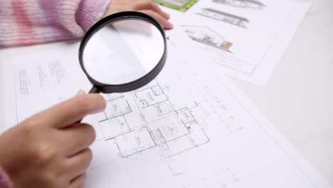 Engineer-using-magnifying-glass-to-examine-architectural-blueprints