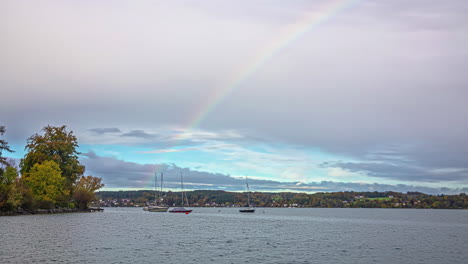 Beautiful-rainbow-above-lake-with-moored-boats,-time-lapse-view