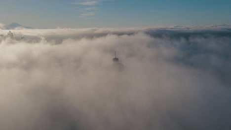Drone-descends-in-sky-above-fog-to-reveal-upper-level-platform-of-iconic-building-with-Mt