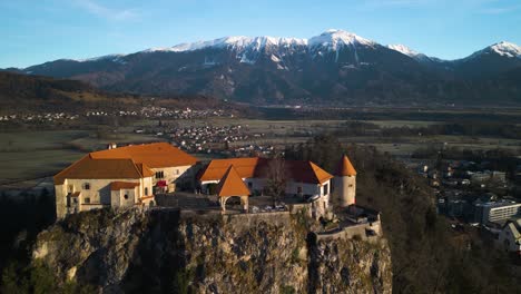 Drone-Flies-Over-Bled-Castle-with-Beautiful-Julian-Alps-in-Background