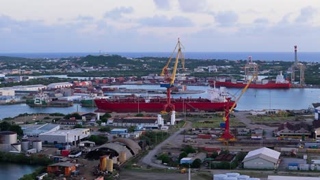 Industrial-seaport-cranes-above-tanker-transit-ship-docked-in-port-at-sunset-on-island