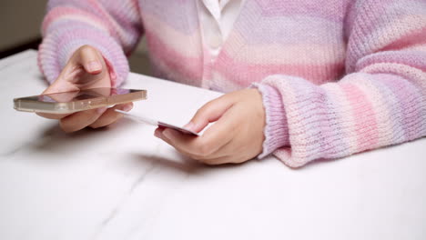 Close-up-woman's-hand-holds-a-smartphone-and-use-a-mockup-Bank-credit-card-for-online-shopping-services-to-pay-money-with-cashless-technology