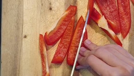 Cutting-a-red-paprika-bell-pepper-on-a-wooden-cutting-board
